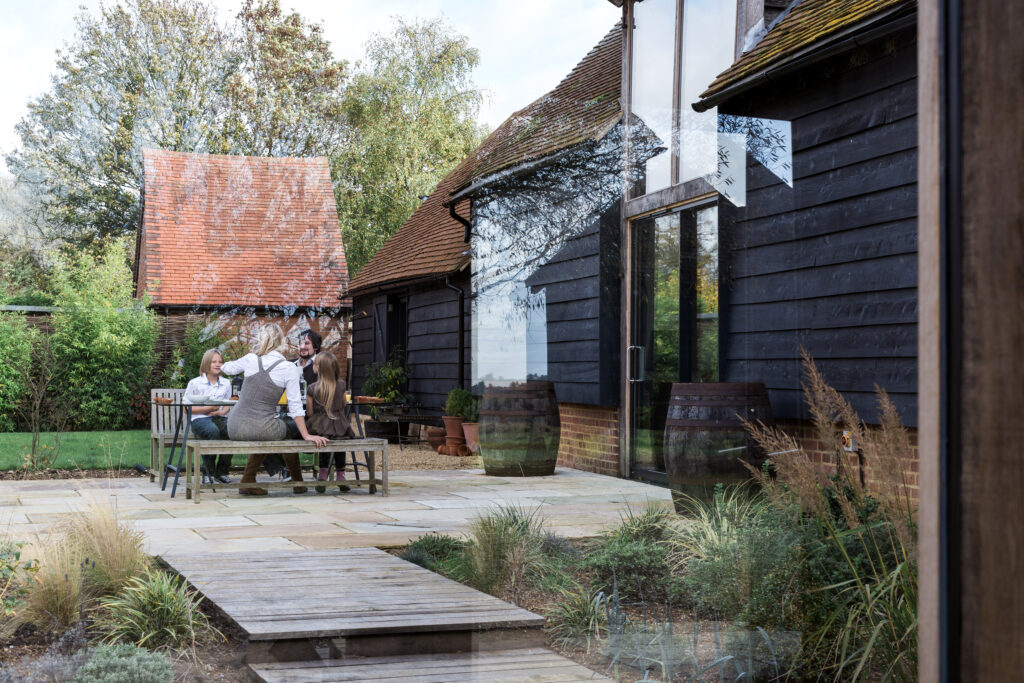Family sitting at bench outside countryside house.